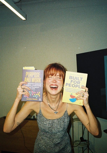 Jessica Zwaan laughing while holding her books Purpose and Work and Built for People